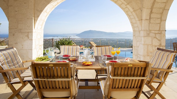 A terrace with a table set for four, overlooking a scenic view of a body of water and mountains. - Luxury stone-made villa with exceptional view & pool (Lefkada)