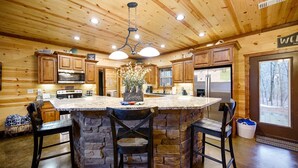 A wooden cabin kitchen with a central island, stone counter, and bar stools. - Luxury Broken Bow Cabin w/ Game Room & Hot Tub | Sleeps 16 (HOCHATOWN)