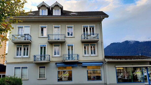 A multi-story building with balconies, large windows, and a mountain backdrop.