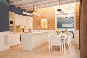 Uma cozinha moderna com armários brancos, uma ilha central e iluminação pendente.