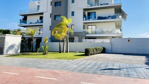 A modern multi-story residential building with balconies, a paved courtyard, and palm trees. - Enjoy the sun, sand and salty sea in a stylish floor on the first line (Torrox)