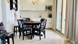 A modern kitchen with white cabinets, a dining table with four chairs, a chandelier, and a large window with curtains. - Enjoy the sun, sand and salty sea in a stylish floor on the first line (Torrox)