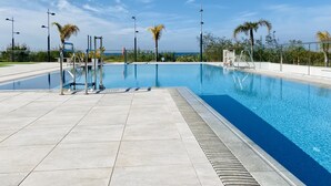A clear blue swimming pool with a tiled deck, surrounded by palm trees and street lamps, under a clear sky. - Enjoy the sun, sand and salty sea in a stylish floor on the first line (Torrox)