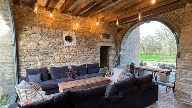 Un espace extérieur aménagé avec des murs en pierre, un plafond en bois, une grande fenêtre et une vue sur un paysage verdoyant.