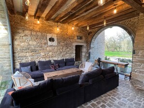 A stone-walled outdoor seating area with a wooden ceiling, a large window, and a view of a green landscape.