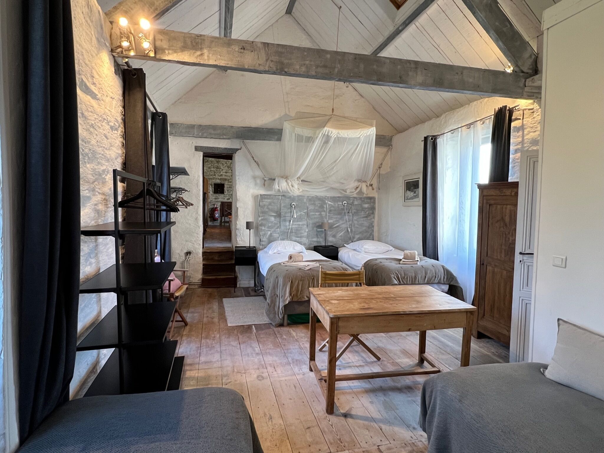 A rustic room with two beds, a wooden table, and a large window.
