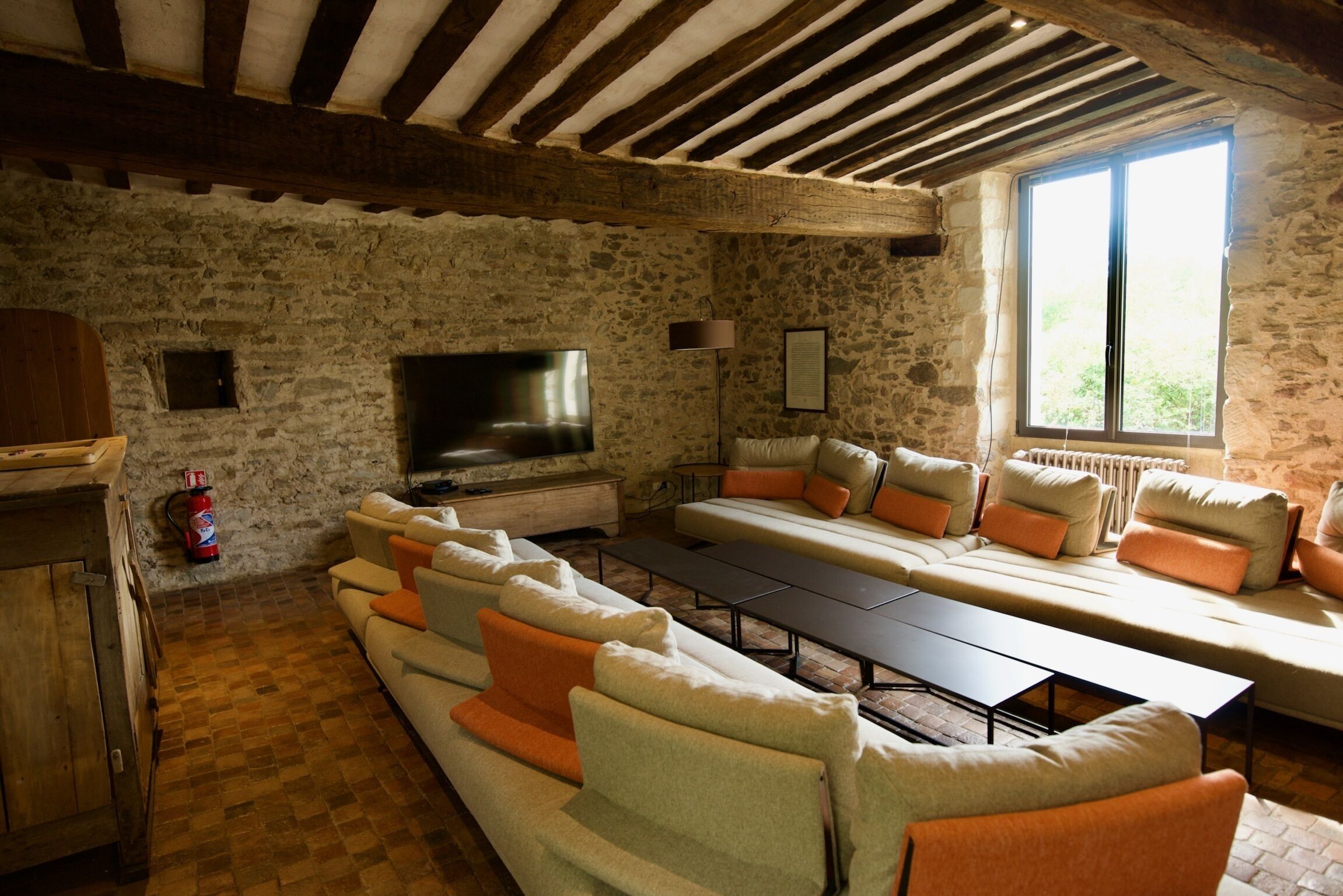 A rustic stone-walled room with a large sofa set, a television, and a window providing natural light.