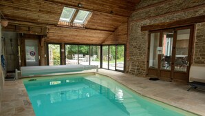 Une piscine intérieure avec un mur en pierre et un plafond en bois, de grandes fenêtres et une vue sur l’extérieur.