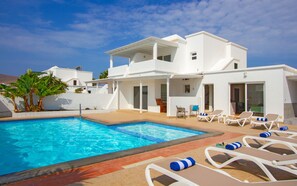 Une villa moderne de couleur blanche, dotée d’une piscine, de chaises longues et d’un espace patio.