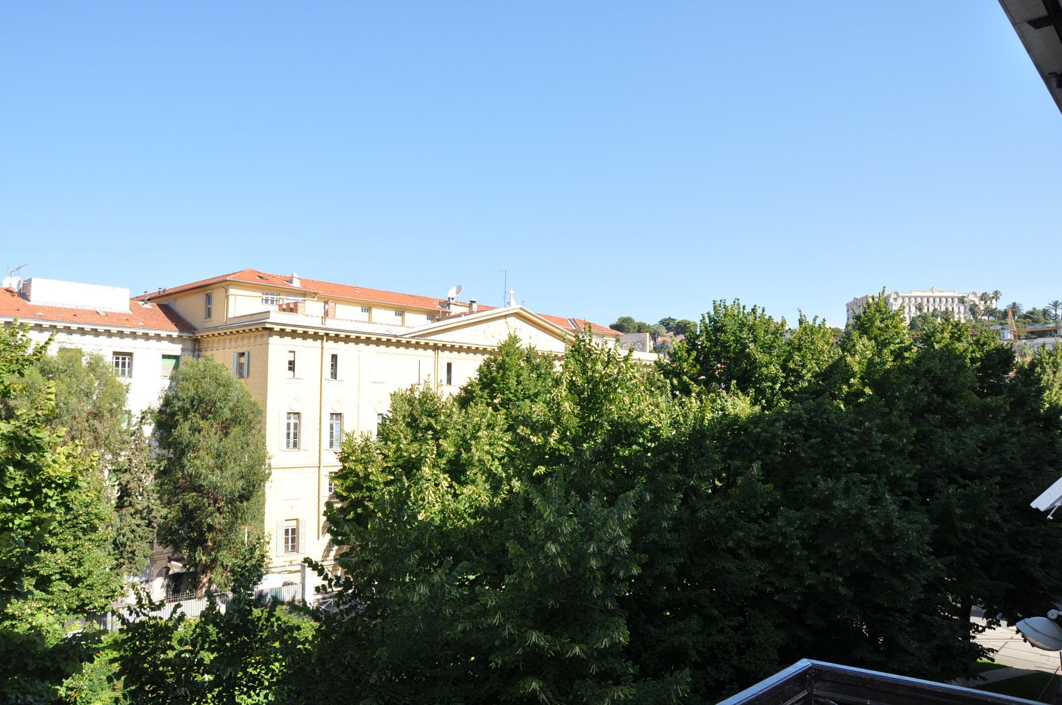 A multi-story building with a red-tiled roof, surrounded by lush green trees.