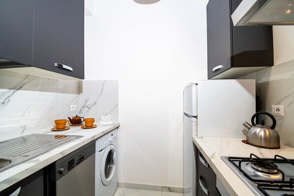 Une cuisine compacte équipée d’un lave-linge, d’une cuisinière à gaz et d’une bouilloire.