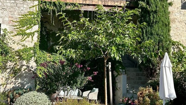 Een gebouw van natuursteen met een balkon, terras en diverse planten.