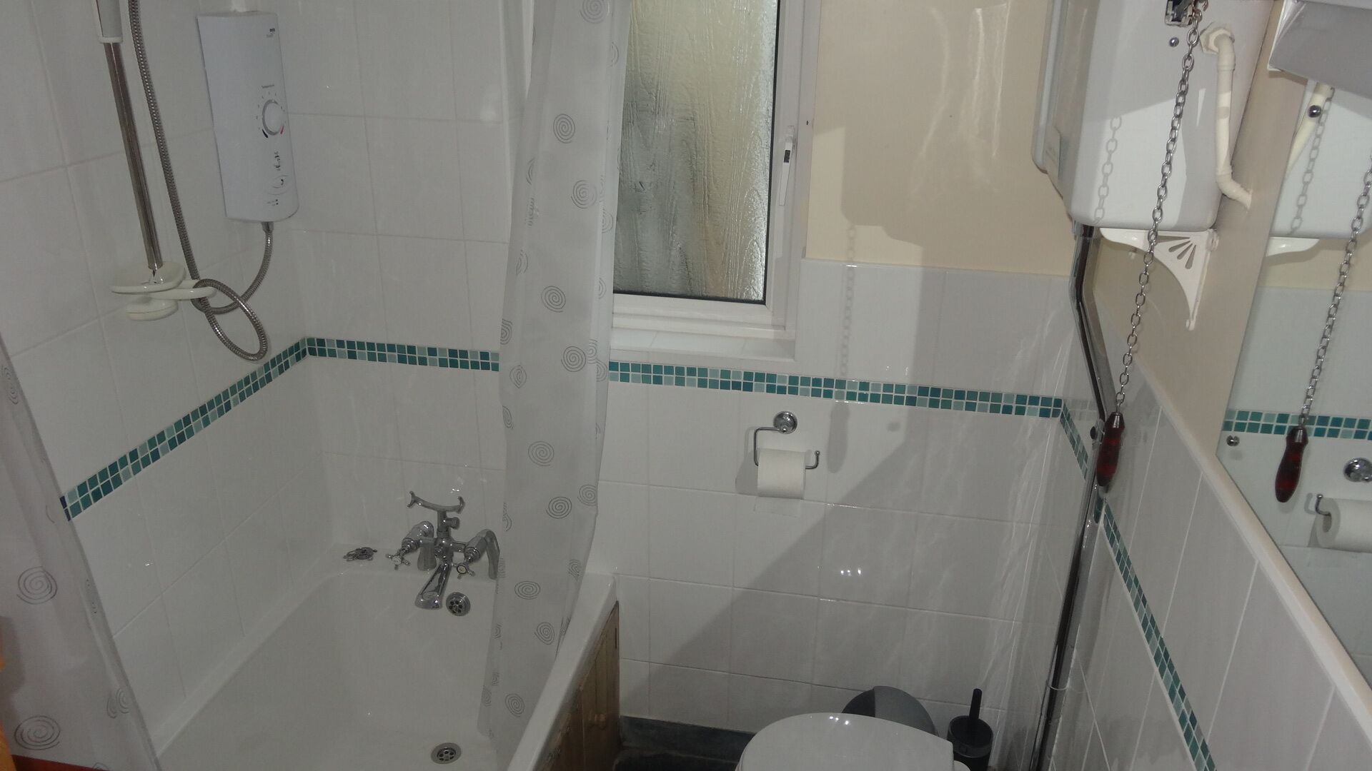 A small bathroom with a shower, toilet, and a window.