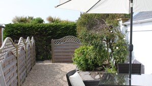 A patio area with a table and chairs, a white umbrella, and a wooden gate. - A Delightful 19th Century Beamed Cottage In Trevone Bay, 3 Mins From The Beach (Padstow)