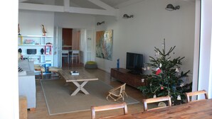 Un vaste espace de vie comprenant un coin repas avec une table en bois, un téléviseur et un sapin de Noël décoré.