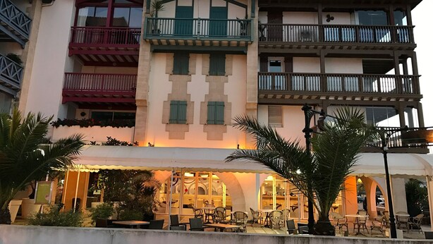 Un immeuble à plusieurs étages doté de balcons, d’un espace extérieur aménagé pour s’asseoir et d’un espace réservé au restaurant.