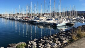 Un port de plaisance où de nombreux voiliers sont amarrés le long du rivage, entouré d’un paysage rocheux et sous un ciel dégagé.