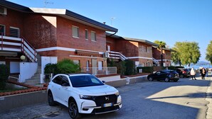 A white SUV parked in front of a brick building with a balcony and a staircase. - Lake Maggiore Apartment (Villaggi)
