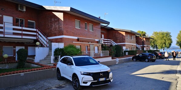 A white SUV parked in front of a brick building with a balcony and a staircase.