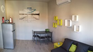 A compact living space with a kitchenette, a dining area, and a seating area with a sofa and cushions. - Lake Maggiore Apartment (Villaggi)