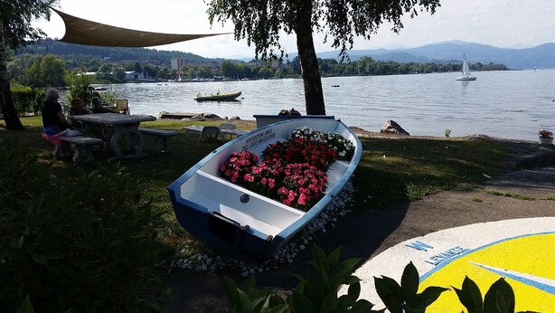 A boat with flowers on a lakeside path, surrounded by picnic tables and greenery. - Lake Maggiore Apartment (Villaggi)
