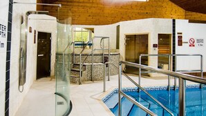 Piscina interna com guarda-corpos de vidro, piso revestido e teto de madeira.