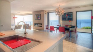 Une cuisine moderne dotée d’un grand îlot central, de chaises rouges et offrant une vue sur la mer.