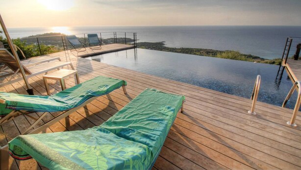 Une piscine à débordement avec des chaises longues et une terrasse en bois offrant une vue sur la mer.