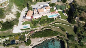 An aerial view of a coastal property with a swimming pool, multiple buildings, and a beach area.