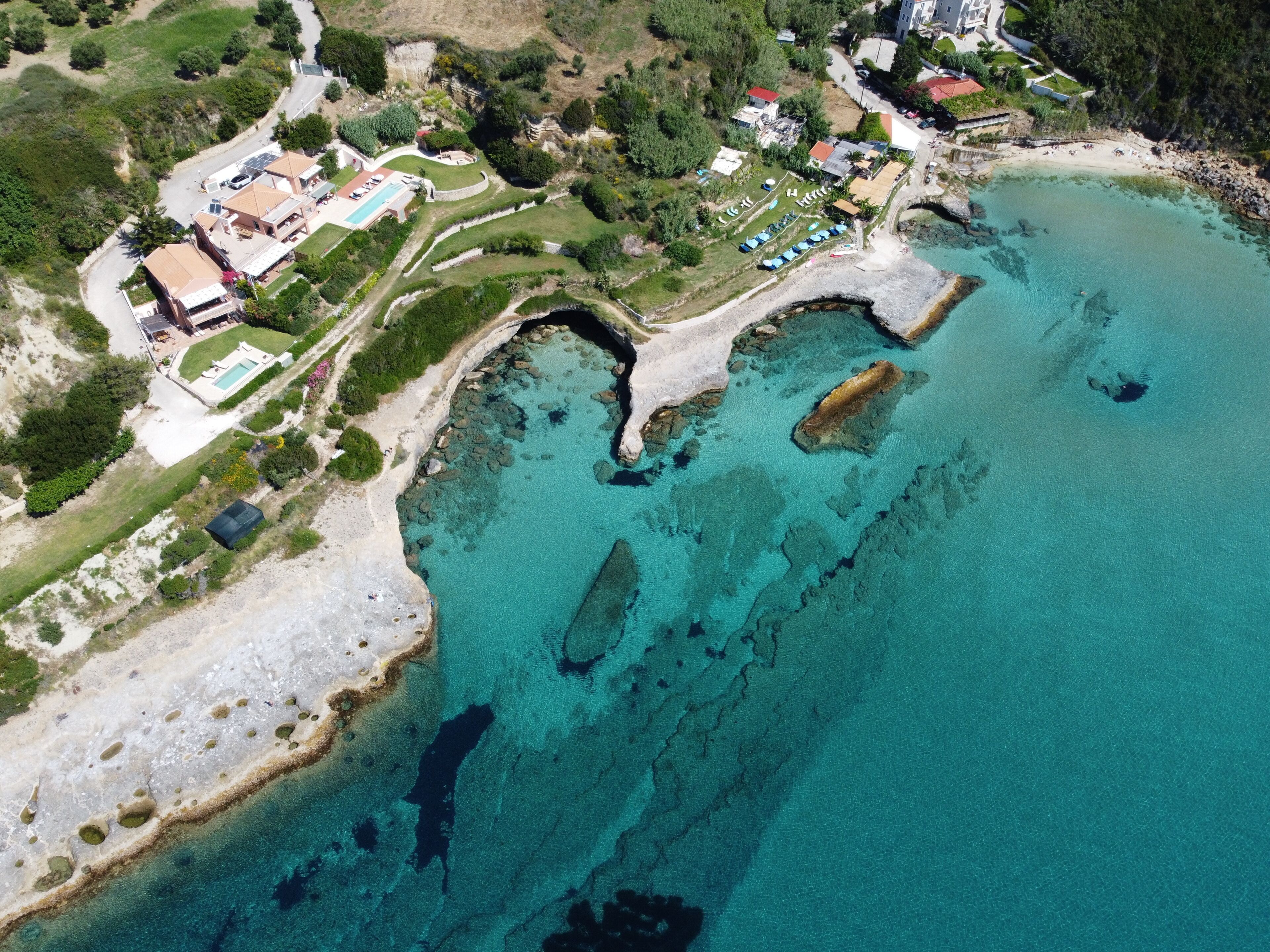 An aerial view of a coastal property with clear turquoise waters, a swimming pool, and a small beach area.