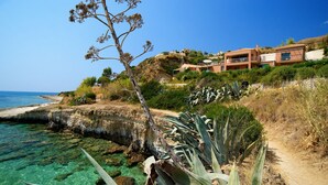 A coastal property with a clear view of the sea, a dirt path, and a building with multiple balconies overlooking the landscape.