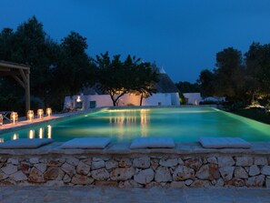 Una piscina con paredes de piedra, un pérgola y un edificio con techo cónico al fondo.