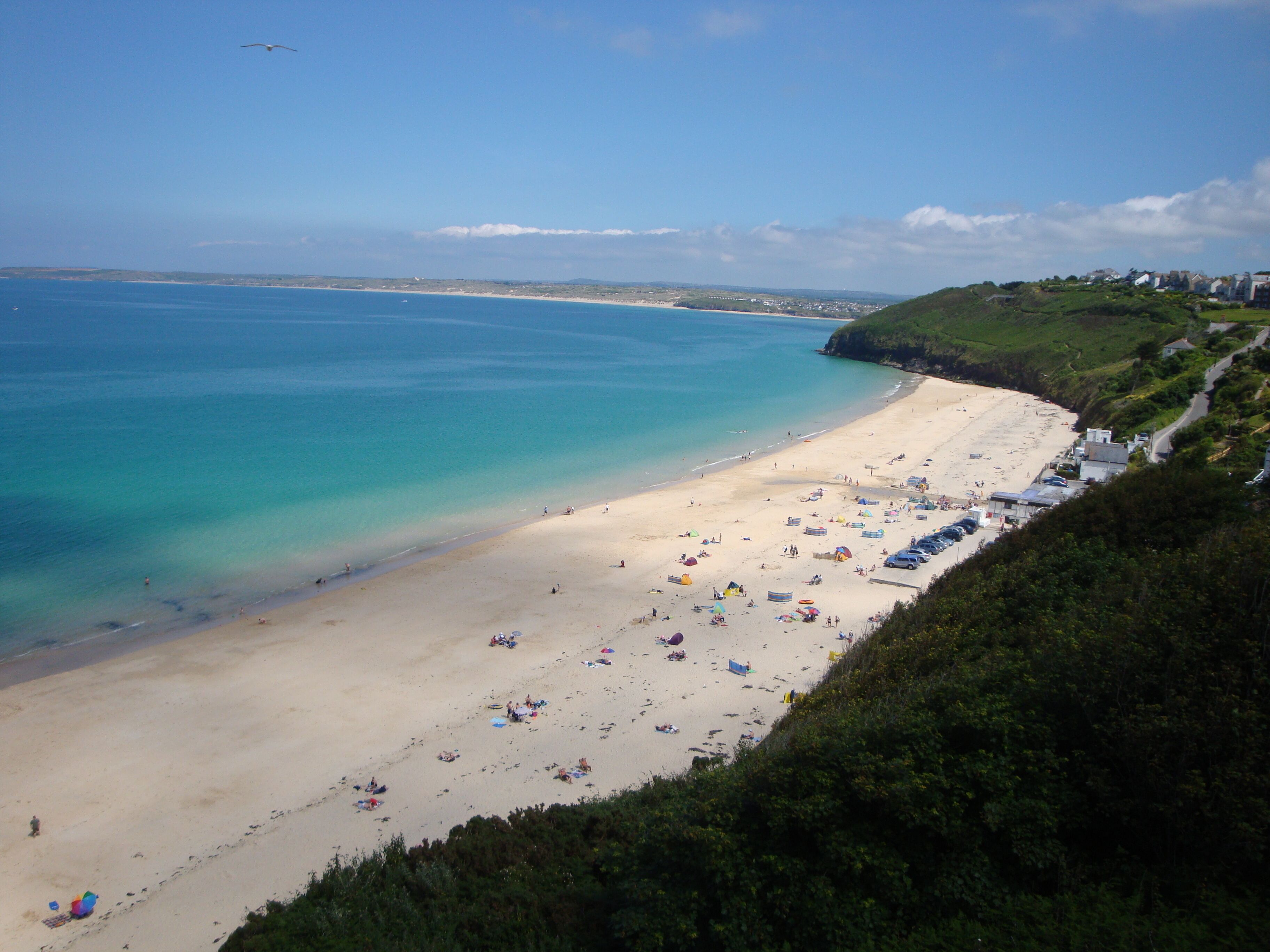 Une plage offrant une vue dégagée sur la mer, une rive sablonneuse et quelques bâtiments visibles au loin.
