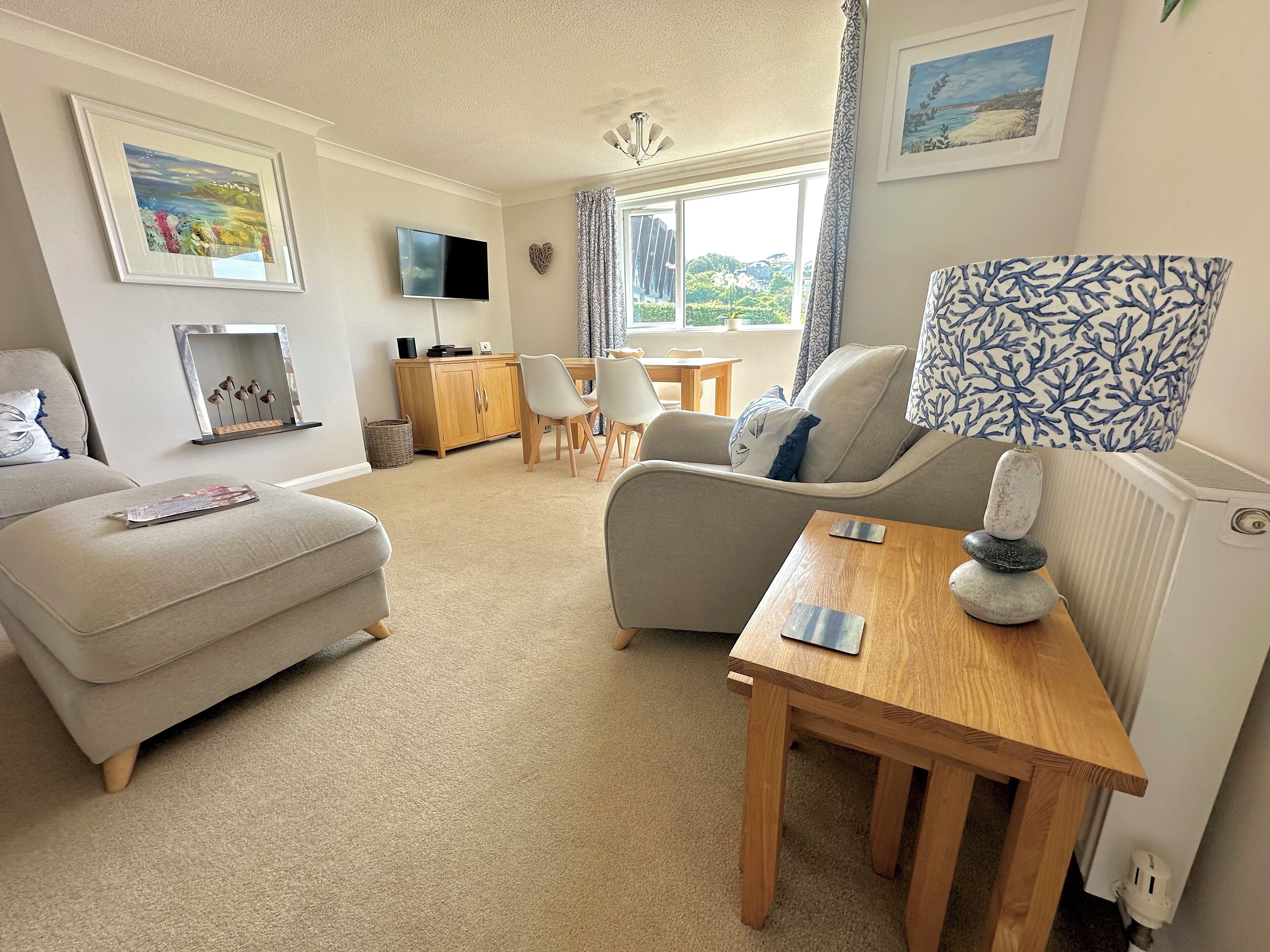 A well-lit living room with a sofa, a dining table, and a TV mounted on the wall.