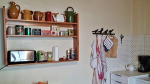 A kitchen with wooden shelves holding various kitchenware, a microwave, and a basket of fruit. - House / Villa - Lescun (Lescun)