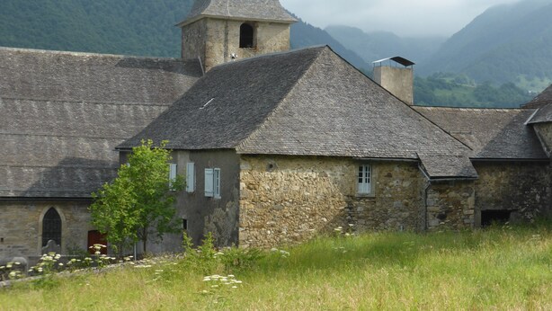 A stone building with a conical roof and a bell tower, surrounded by a grassy field and mountains in the background. - House / Villa - Lescun (Lescun)