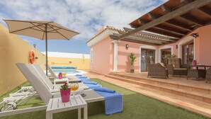 A poolside area with lounge chairs, a table with a drink, and a covered patio with wicker furniture. -  VILLA "BELLA LUCIA 1" PRIVATE HEATED POOL, WIFI, BARBECUE, SATELLITE TV  (corralejo- la oliva)