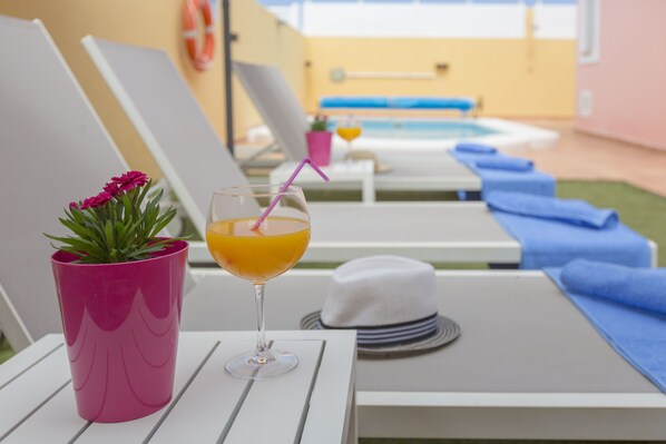 A poolside area with lounge chairs, a drink in a pink cup, and a white hat on a table. - VILLA "BELLA LUCIA 1" PRIVATE HEATED POOL, WIFI, BARBECUE, SATELLITE TV (corralejo- la oliva)