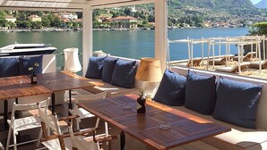 A sunlit outdoor seating area with a view of a lake and mountains. - “For a perfect and UNFORGETTABLE GIFT … (Sala Comacina)