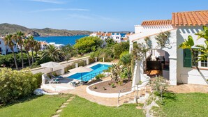 A residential area with a swimming pool, white buildings, and a view of the sea. - Casa Lavanda (Fornells, Menorca)