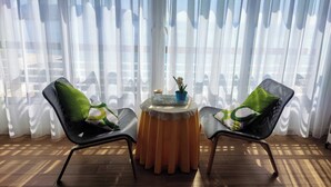 Ein Zimmer mit zwei Stühlen, einem runden Tisch und durchsichtigen Vorhängen.