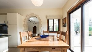 A dining area with a wooden table and chairs, a blue bowl, and a stone archway leading to a kitchen. - Beautiful Stone Villa with large pool, close to beaches plus free use of car : ) (Coral Bay, Peyia)
