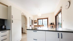 A modern kitchen with white cabinets, a black countertop, and a stone archway leading to a dining area. - Beautiful Stone Villa with large pool, close to beaches plus free use of car : ) (Coral Bay, Peyia)