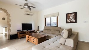 A living room with a sofa, coffee table, TV, and a ceiling fan. - Beautiful Stone Villa with large pool, close to beaches plus free use of car : ) (Coral Bay, Peyia)