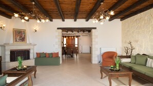 A spacious living room with a fireplace, wooden ceiling beams, and a view into the dining area. - Kalypso Villa, a Serene Family Retreat with Pool (Rethymno)