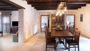A spacious dining area with a wooden table and chairs, a hanging light fixture, and a view into the kitchen. - Kalypso Villa, a Serene Family Retreat with Pool (Rethymno)