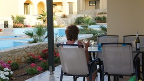 Una persona sentada a una mesa con vista a la piscina, rodeada de asientos exteriores y muros de piedra.