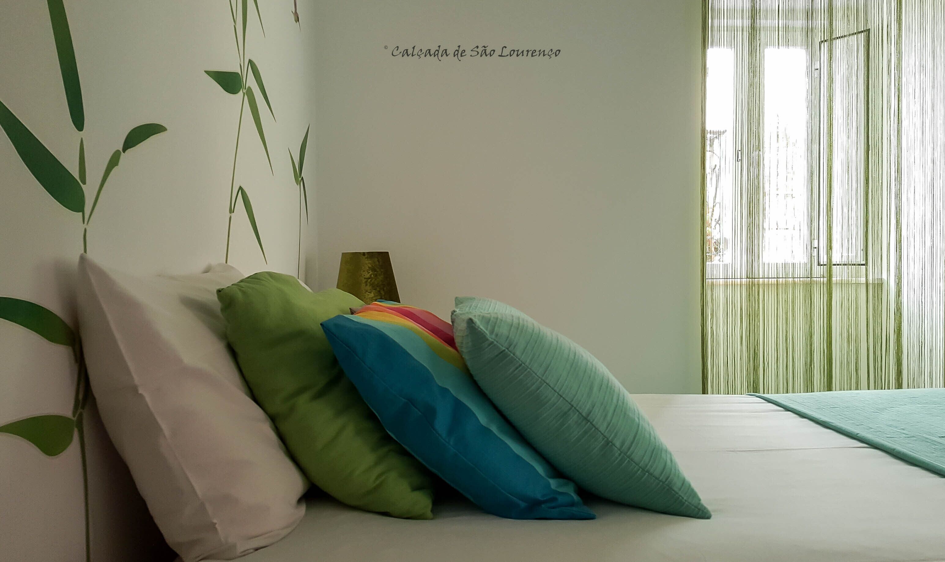Quarto com cama, almofadas, mesa de cabeceira e parede com desenho de planta.