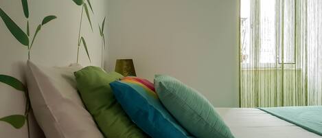 Quarto com cama, almofadas, mesa de cabeceira e parede com desenho de planta.