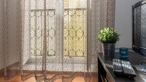 Una ventana con un cortinero de encaje, una planta en maceta y dos controles remotos sobre una superficie negra.
